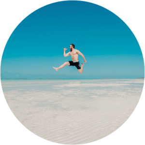 Hombre saltando en una playa con el torso y piernas depiladas